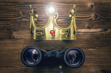 VIP premium search. Binoculars and golden crown on wooden desk table background. In searhing for...