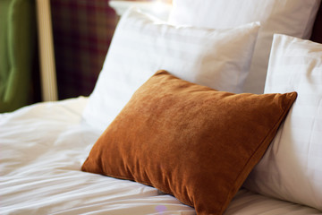 Fototapeta na wymiar Brown pillow on a white bed in apartments. Rest and comfort.