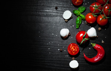 food background. red chili peppers, cherry tomato, basil, black pepper, mozzarella balls, salt on dark wooden background with copy space. top view
