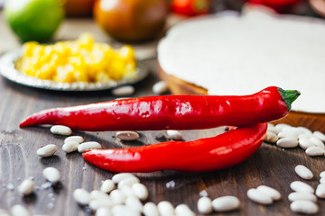 Chili peppers on wooden table, surrounded by beans and vegetables.