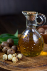 Natural macadamia oil in a glass bottle with macadamia nuts on wooden board.