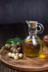 Natural macadamia oil in a glass bottle with macadamia nuts on wooden board.