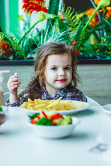 Little cute girl sitting in a restaurant and eating french fries.