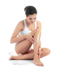 Fototapeta premium Young woman applying body cream on her leg against white background