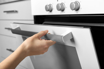 Young woman opening door of modern oven in kitchen