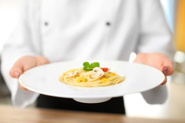 Female chef holding plate with tasty pasta, closeup