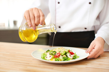Female chef preparing tasty salad in kitchen, closeup