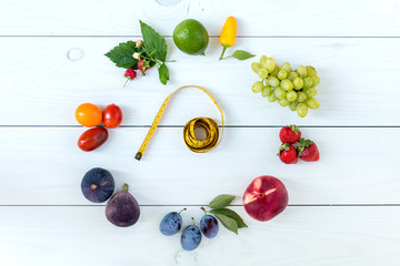 Fototapeta na wymiar Fitness healthy food on white wooden background (lime, strawberry, plum, figs, raspberries, grapes, peppers, peaches, tomatoes nectarines and measuring tape)