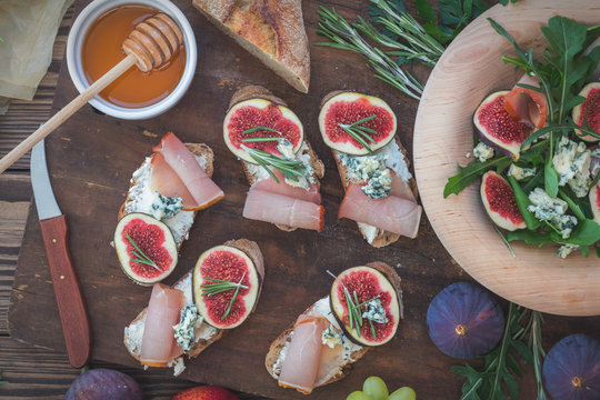 Easy diet salad with arugula, figs and blue cheese on a brown wooden surface. Sandwiches with ricotta, fresh figs, prosciutto, rosemary and blue cheese. Delicious fruity breakfast, top view. Toned.