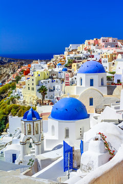 Oia town, Santorini island, Greece at sunset. Traditional and famous white houses and churches  with blue domes over the Caldera, Aegean sea.
