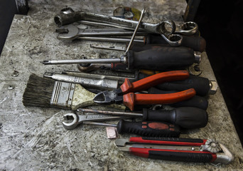An untidy workbench full of greasy old tools set for repairing or maintenance hanging or laying on a bench in a garage