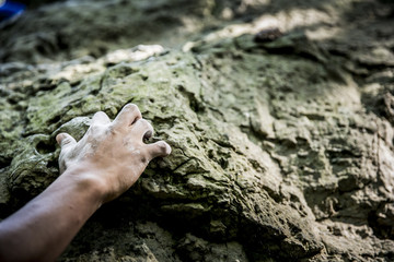 A rock climber reaches up to find a hold in the jagged rocks on a cloudy afternoon in the fall.