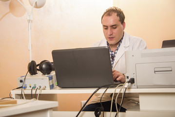 Young doctor doing some work on his laptop in his office, clinic work