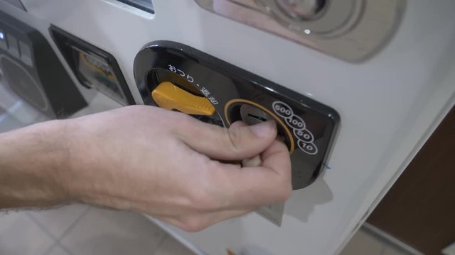 Inserting coins into a vending machine closeup.