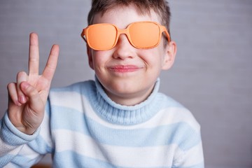 Cute smiling boy in orange sunglasses with opaque lenses showing victory gesture