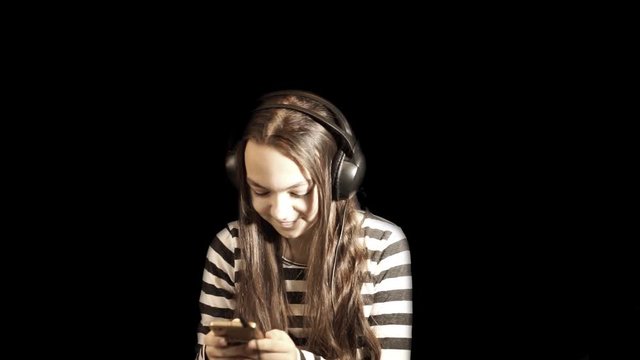 Teenager girl listens to music in headphones and gestures dancing, against a black background. Close up portrait, with a drawn animation of notes icons that go in different directions.