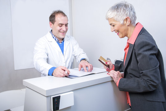 Senior Woman Paying Her Medical Bill At The Clinic With Her Credit Card