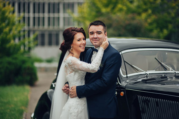 stylish bride and groom sensually posing near retro car with boh