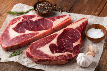 Two fresh raw marble meat, black Angus ribeye steak with spices on a old rustic table. Raw beef on a wooden background