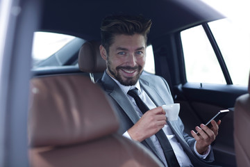 Fototapeta na wymiar Businessman drinking coffee in car with phone in hand