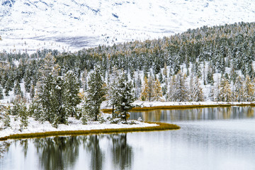 Landscape with a mountain lake in winter. Snow-covered forest on the shore of the lake.