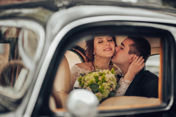 Happy stylish newlywed couple posing in retro car