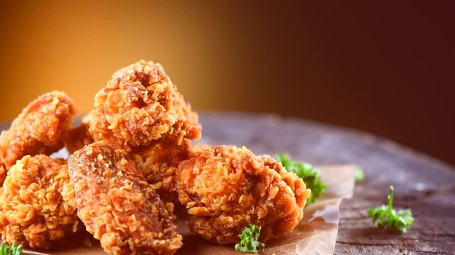 Bucket full of crispy fried chicken rotated on wooden background. 4K UHD video footage. 3840X2160