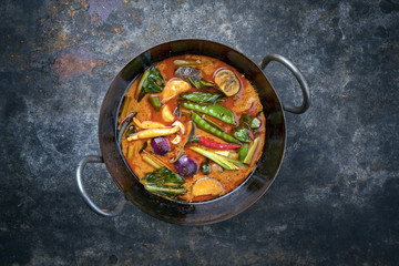 Traditional Thai kaeng phet red curry with vegetables as top view in a wok with copy space