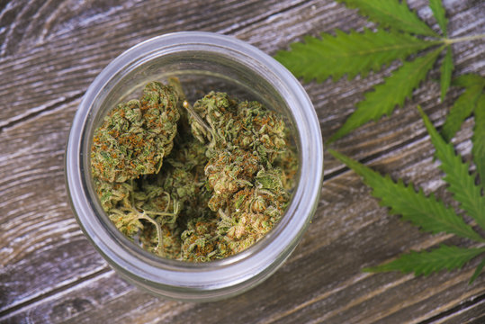 Cannabis buds (scout master strain) on glass jar over wood background