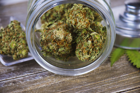 Cannabis buds (scout master strain) on glass jar over wood background