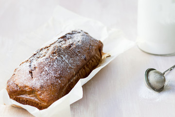 Whole banana bread on baking sheet and tea strainer with icing sugar