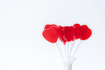 Handful of red heart shaped lollipops standing in white vintage vase with white background