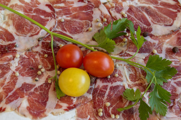 Texture of Italian delicacy dried meat with spices, cherry tomatoes and sprig of parsley.