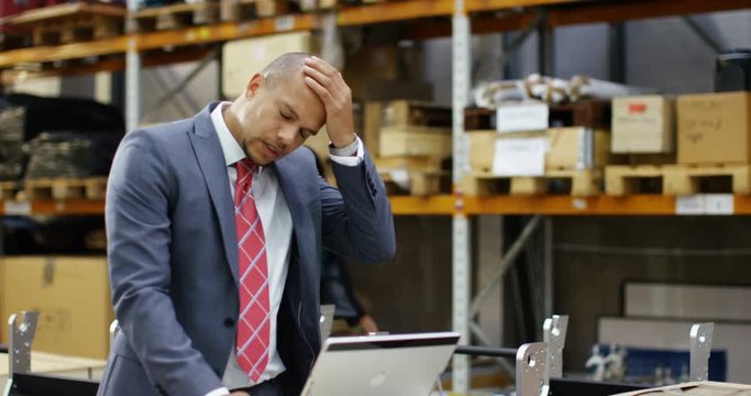 4k, Tired businessman with a concerned look working at a large warehouse.