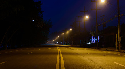 Fototapeta na wymiar Empty street at early morning before dawn shrouded in mist illuminated by streets lights