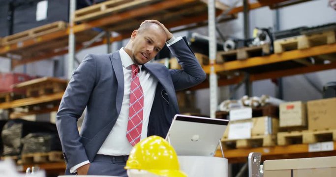 4k, Tired businessman with a concerned look working at a large warehouse.