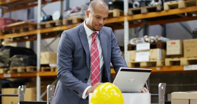 4K Cheerful businessman working on laptop in large industrial warehouse