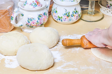 Woman rolls wheat raw dough with a rolling pin