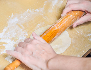 Woman rolls wheat raw dough with a rolling pin