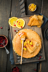 English-style pancakes with lemon, fresh berries and honey on a wooden dark cutting board, traditional for Shrove Tuesday. Happy Shrovetide!  And Maslenitsa - Russian traditional spring festival. 