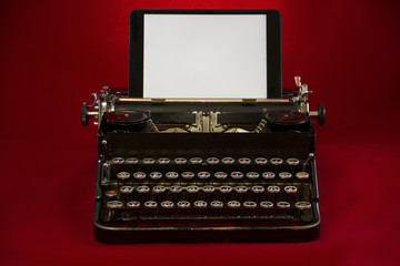 Alte Schreibmaschine mit weißem Tablet-Display und rotem Hintergrund
