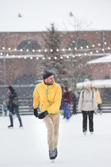 Full length portrait of joyful bearded man in yellow jacket, beige trousers, black hat on ice rink, outdoors in snowy winter day/ Weekend activities outdoor in cold weather/Winter time concept