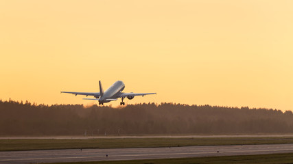 Fototapeta na wymiar Airplane taking off against the sunset above a runway, copy space, horizontal, back view/ plane fly up at sunset yellow sky/silhouette of airplane in sunset sky/ Vacation, aviation and travel concept