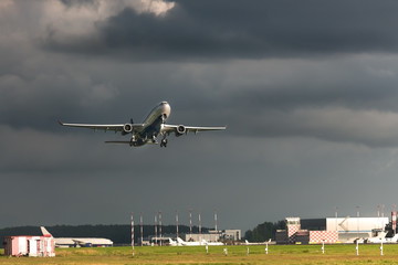 Fototapeta premium Airplane taking off in summer day front view, horizontal, rain clouds on background/ Plane fly up at cloudy day/ Take off a wide-body aircraft from the airport/ Vacation and travel concept, copy space