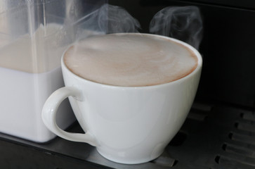 Cappuccino coffee white cup  with steam at coffee machine background