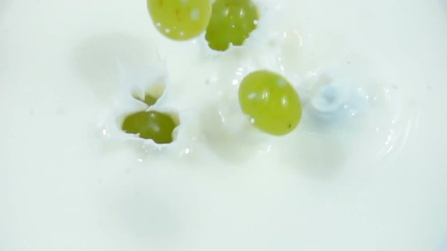 Berries of green grapes are dropped into fresh white milk in slow motion.