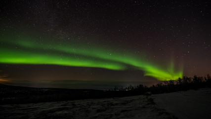 Green Northern Lights (Aurora Borealis) above frozen lake Tornetraesk in northern most part of Sweden. Clear starry sky dominated by the green northern light filing almost the full picture.