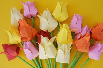 Tulips of origami from multi-colored paper on a yellow background