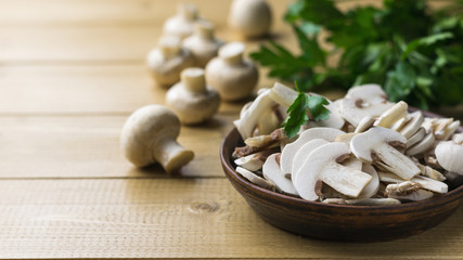 Fresh sliced mushrooms in a clay bowl and parsley on a wooden table.