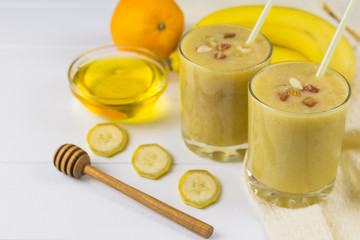 Freshly made smoothies with mango, banana, orange, honey, nuts and cereal on a white wooden table.